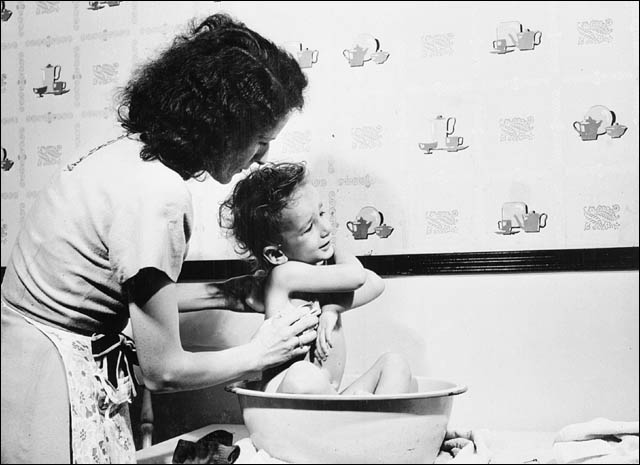 Typical Canadian family, Mrs. William Meadows of Hull, gives 3 year old Gary a bath in the kitchen of their four room apartment