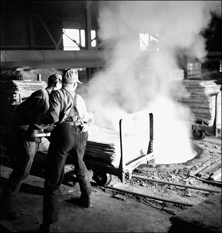 Workmen throw an electrolytic sheet of zinc into a melting furnace at the Consolidated Mining & Smelting Company of Canada Ltd