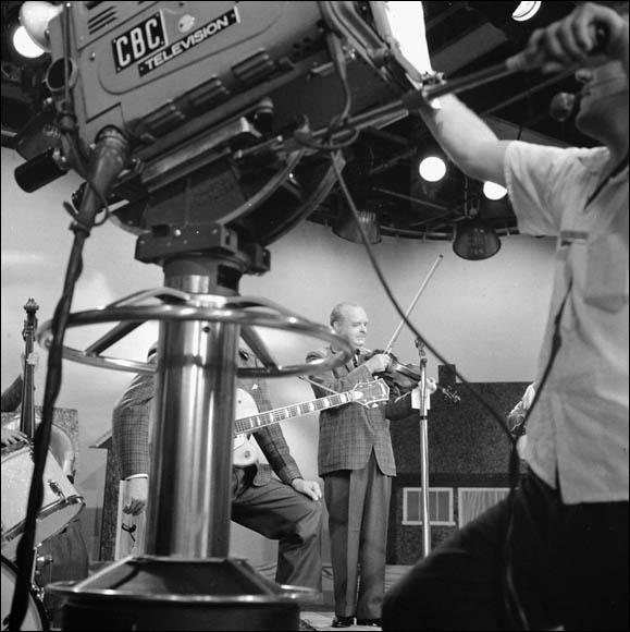 Entertainer-fiddler Don Messer seen through television equipment during production of the Don Messer and His Islanders show